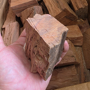 Hand holding a Pimento Wood Chunk from 1kg pack for Smoking & Jerking. Ideal size and density for slow-burning, flavorful outdoor grilling.