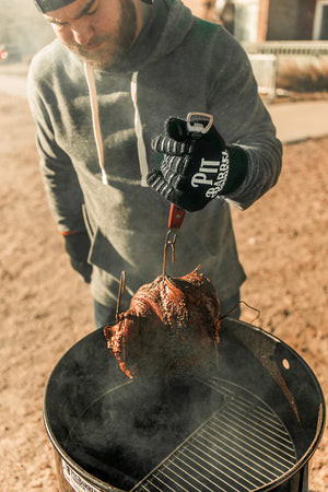 Griller lifting smoked meat with Pit Barrel Ultimate Hook Tool - FireFly Barbecue, designed for safe and efficient outdoor cooking.