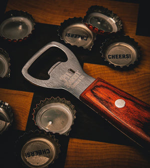 Close-up of Pit Barrel Ultimate Hook Tool - FireFly Barbecue surrounded by bottle caps, emphasizing its bottle opener feature.