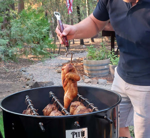 Man lifting whole chicken from Pit Barrel PBX 22.5 Cooker using hook, ideal for outdoor BBQ and vertical smoking.