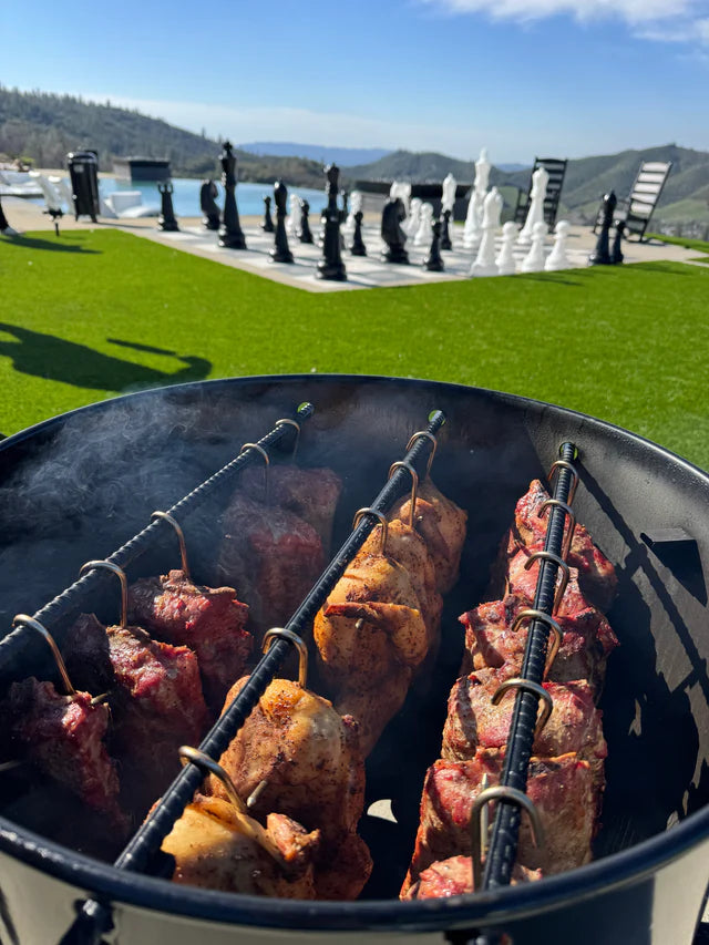 Meat skewers cooking on outdoor Pit Barrel smoker with scenic background