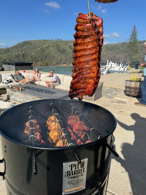 Grilled ribs being lifted from Pit Barrel PBX Cooker, demonstrating its effectiveness in smoking and grilling large meat portions outdoors.