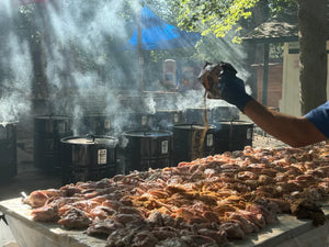 Outdoor BBQ setup with multiple Pit Barrel PBX Cookers and a table full of seasoned meat, perfect for large gatherings or competitions.