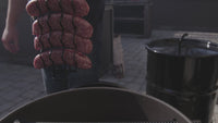 Sausages hanging on hooks above Pit Barrel Hinged Grate, demonstrating vertical smoking capability in outdoor barbecue setup.