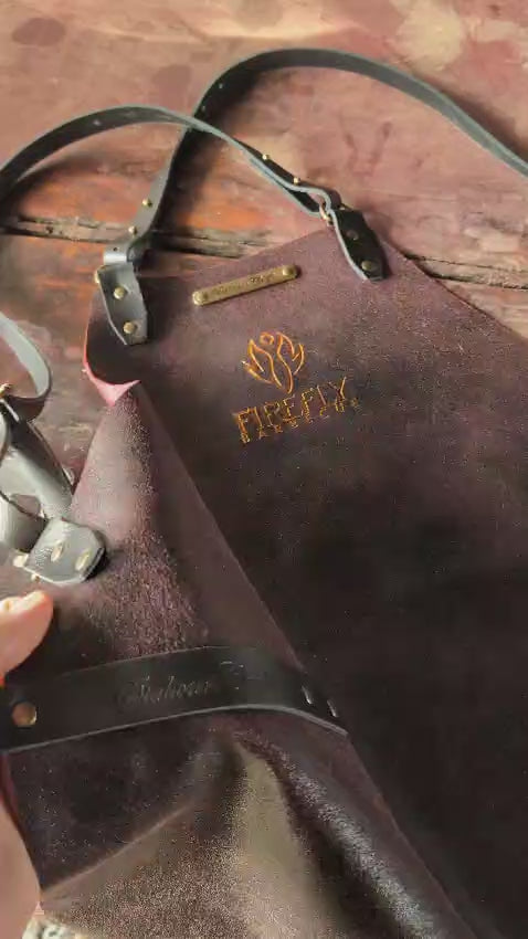 Detailed view of FireFly Barbecue leather apron showing embossed logo, cross-strap attachment, and high-quality leather grain.
