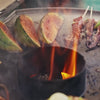Outdoor grilling scene with sliced fruit, skewered meat, and flames on Kamado grill for outdoor cooking