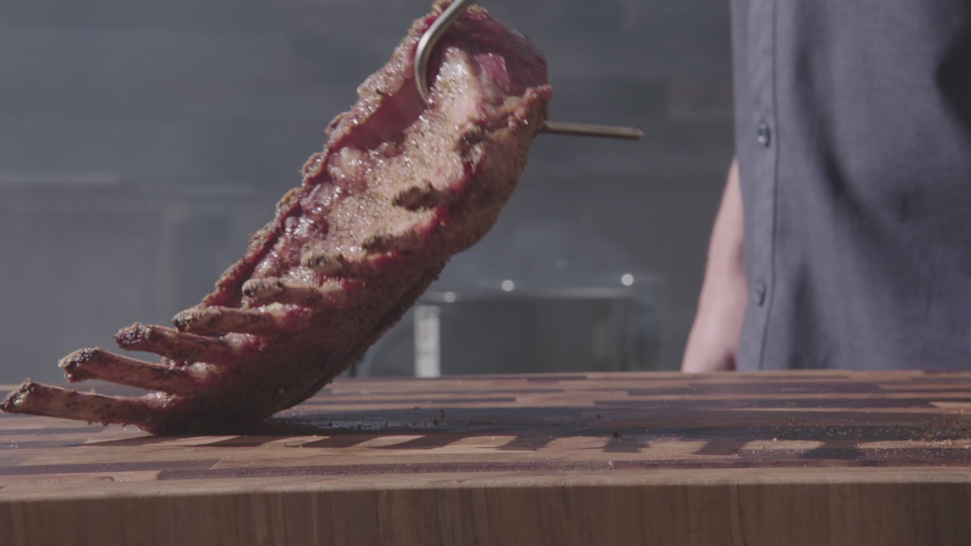 Pit Barrel Ultimate Hook Tool - FireFly Barbecue lifting a rack of ribs from cutting board, perfect for handling hot meats on the grill.