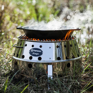 Petromax 30cm Cast Iron Fire Skillet with Two Handles placed on a Petromax Atago grill, steaming over a live fire in a grassy outdoor setting.