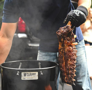 Man lifting smoked ribs from Pit Barrel Junior grill smoker using gloves. Ideal for outdoor cooking and camping with vertical hanging method.