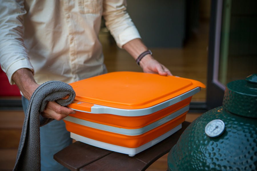 Person cleaning BBQ prep tub with towel before outdoor grilling