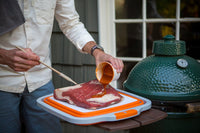 Person seasoning meat on BBQ prep tub with built-in cutting board