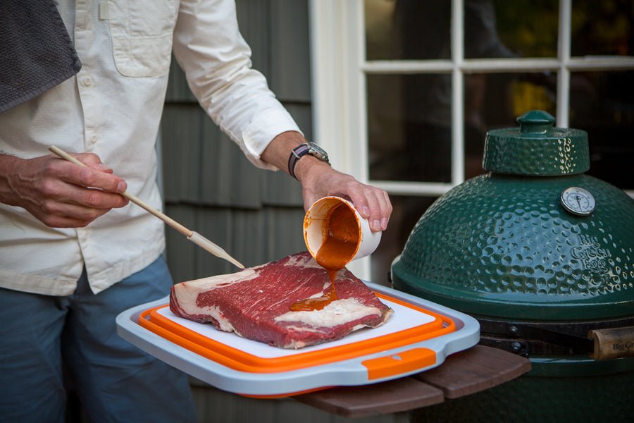 Person seasoning meat on BBQ prep tub with built-in cutting board