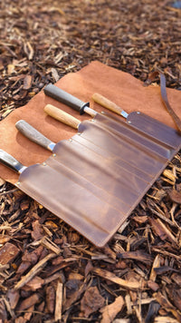 Set of outdoor knives in leather roll on wood chips
