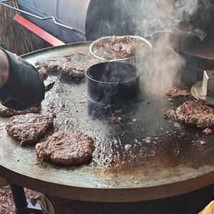 Monolith Fire Plate - Classic in use with burgers and onions grilling on hot steel surface, ideal outdoor BBQ accessory by FireFly Barbecue