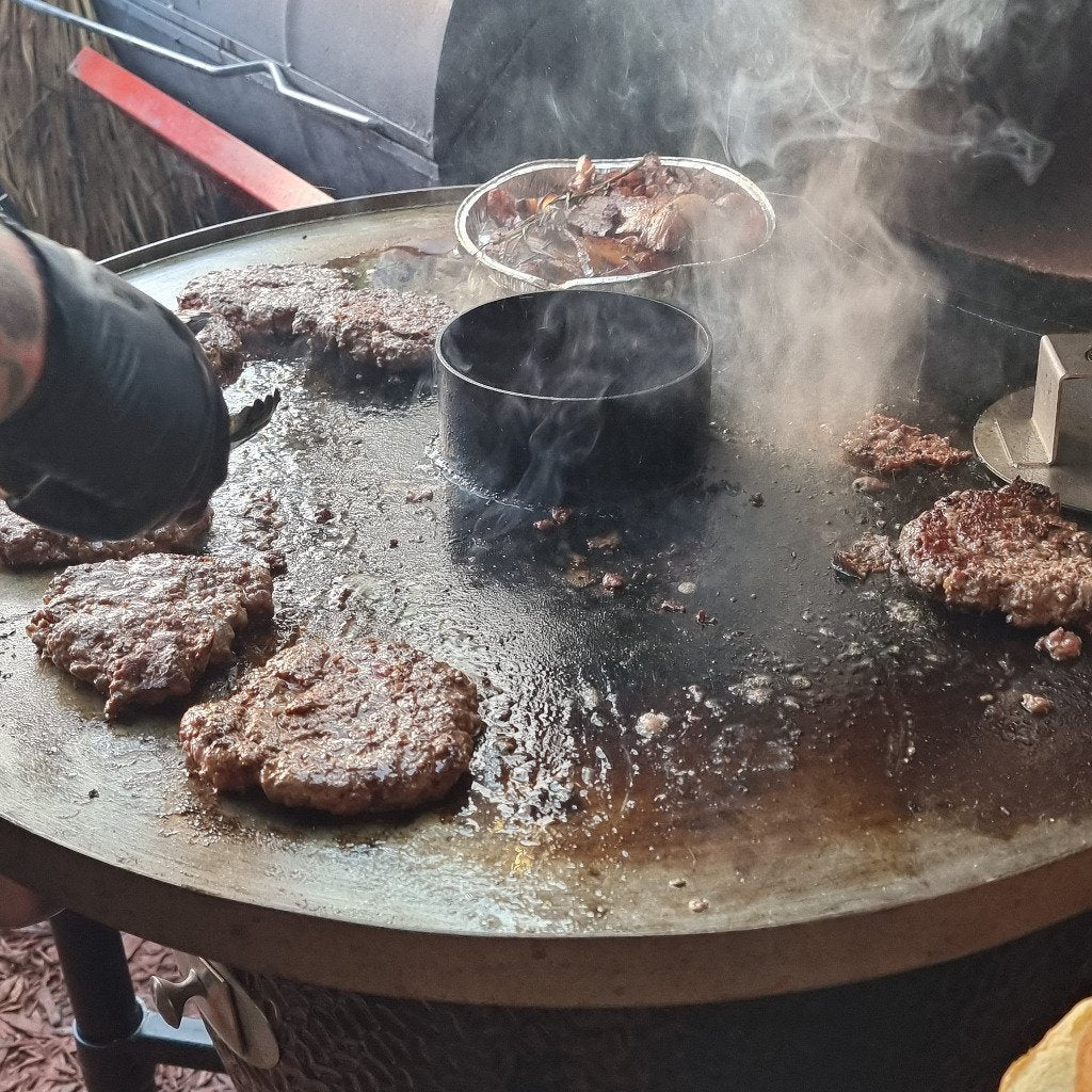Juicy burgers sizzling on Monolith Fire Plate - Icon, demonstrating high-heat searing and versatile outdoor grilling performance.