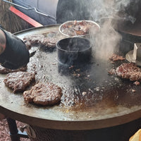 Juicy burgers sizzling on Monolith Fire Plate - Icon, demonstrating high-heat searing and versatile outdoor grilling performance.
