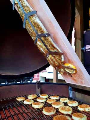 Seasoned salmon fillet secured on Monolith Fish Plank - Beech, grilling vertically over ceramic grill with sliced vegetables below.