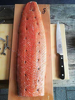 Whole salmon fillet seasoned and placed on Monolith Fish Plank - Beech, ready for grilling with included stainless steel clamp.