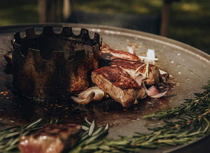 Steak and onions cooking on a steel fire plate atop the MONOLITH Icon Kamado Grill, ideal for Teppanyaki-style outdoor grilling.