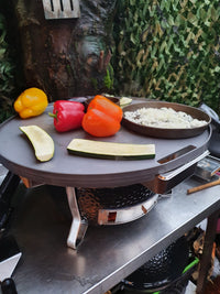 MONOLITH Icon Kamado Grill used as a tabletop Plancha grill with vegetables and rice cooking on a steel fire plate outdoors.