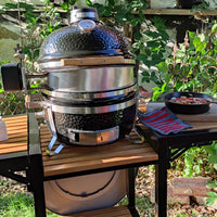 Black Monolith rotisserie grill on wooden table with garden background