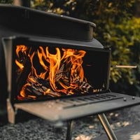 Open firebox of Ozpig Big Pig BBQ stove with roaring flames, designed for outdoor cooking and heating versatility.