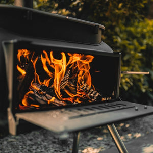 Open firebox of Ozpig Big Pig BBQ stove with roaring flames, designed for outdoor cooking and heating versatility.