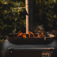 Ozpig Big Pig BBQ stove with open top and visible flames, designed for outdoor heating and grilling experiences.