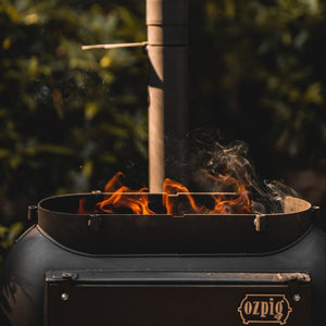 Ozpig Big Pig BBQ stove with open top and visible flames, designed for outdoor heating and grilling experiences.