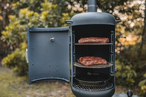 OzPig Oven Smoker with ribs and drip tray inside, set in a garden. Designed for outdoor BBQ and roasting with stable heat control.