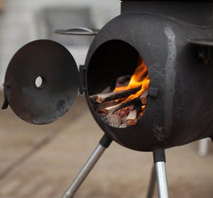 Ozpig Series 2 Portable Wood Fired BBQ Stove with firewood burning inside, ideal for backyard cooking and outdoor warmth.