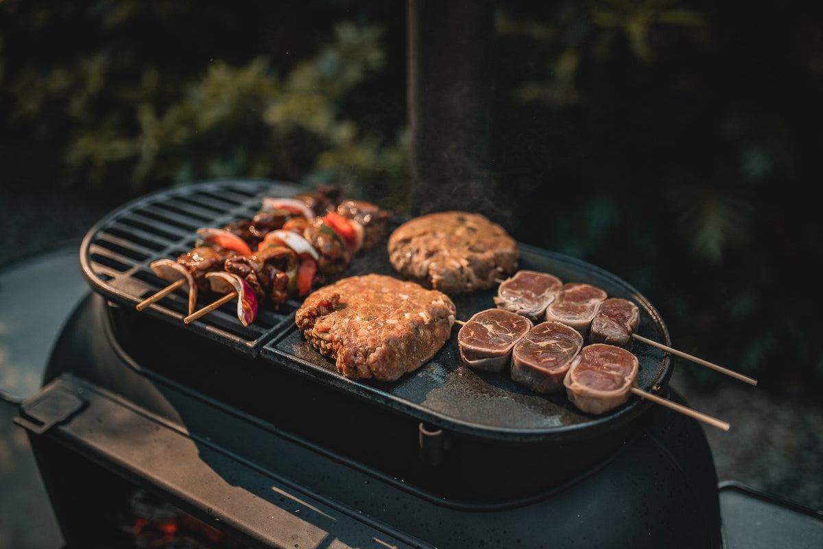 Outdoor grill with skewers, burger patties, and lamb chops cooking at night