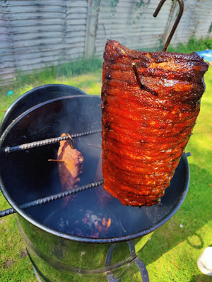 Juicy ribs hanging inside Pit Barrel Classic Cooker Standard over hot coals, demonstrating its vertical drum smoker efficiency.