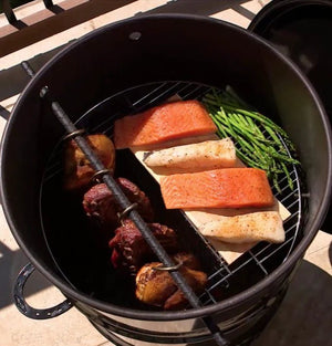 Top view of Pit Barrel Classic Cooker Standard grilling salmon, asparagus, and meat, highlighting its spacious cooking area.