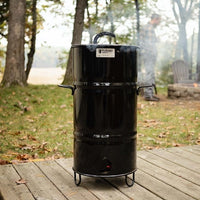 Black outdoor barrel smoker on wooden deck in nature setting