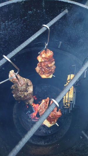 Inside view of Pit Barrel Junior smoker with meat and corn hanging over charcoal fire. Compact grill ideal for flavorful vertical smoking.