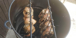 Chicken halves hanging inside Pit Barrel Junior smoker over hot coals. Efficient vertical cooking system for juicy, smoked meats outdoors.