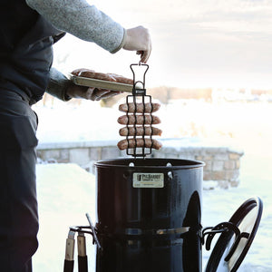 Sausages being lowered into a Pit Barrel Cooker using Pit Barrel Sausage, Hot Dog & Brat Hanger - FireFly Barbecue for outdoor smoking.